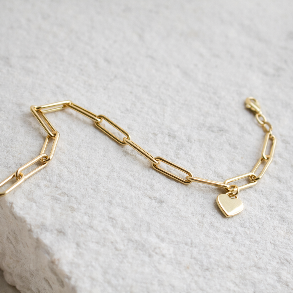10k gold paperclip bracelet with heart charm on white stone