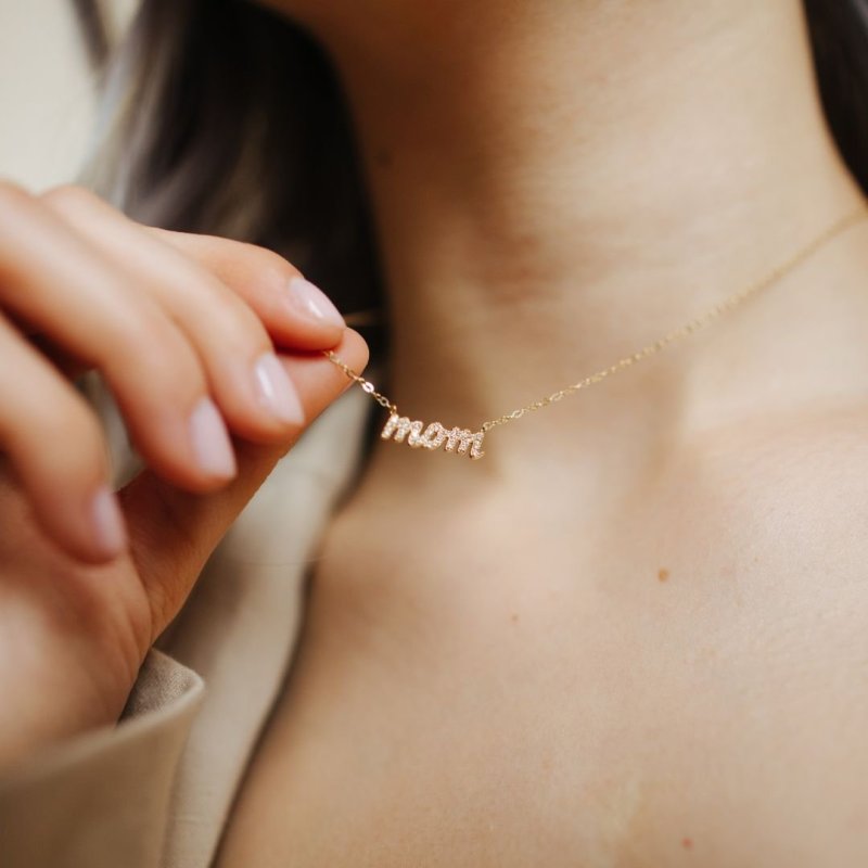 Gold 'mom' necklace being worn on a person's neck