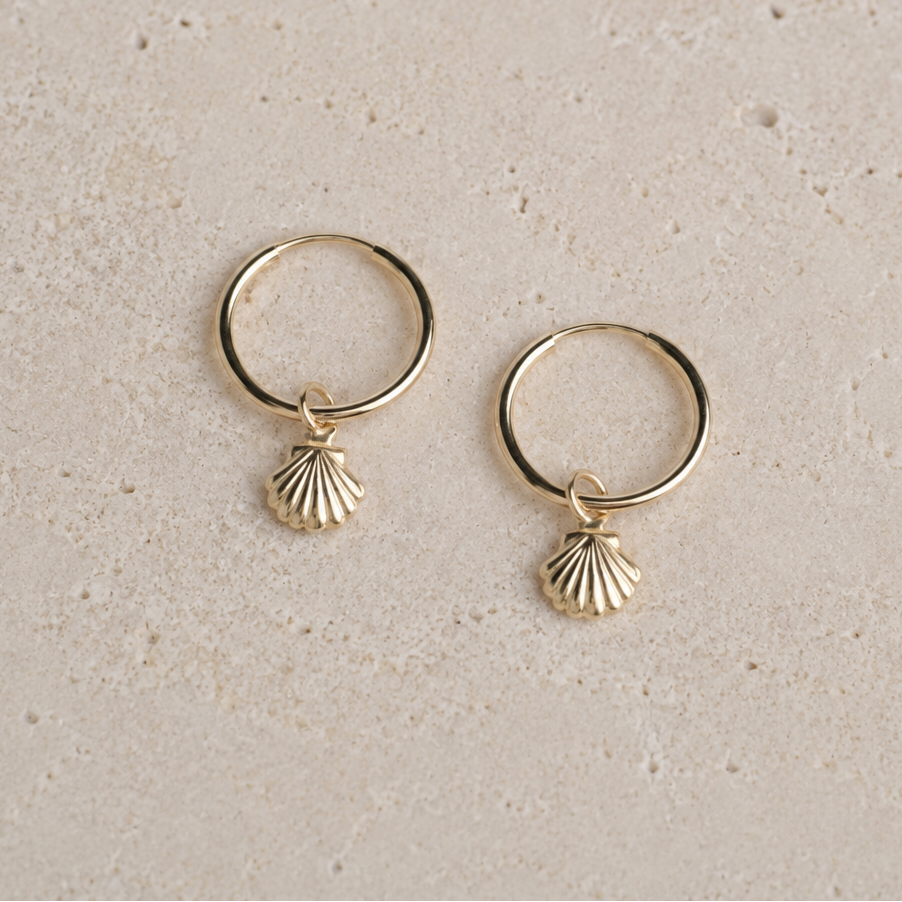 Gold hoop earrings with shell charms on a beige background