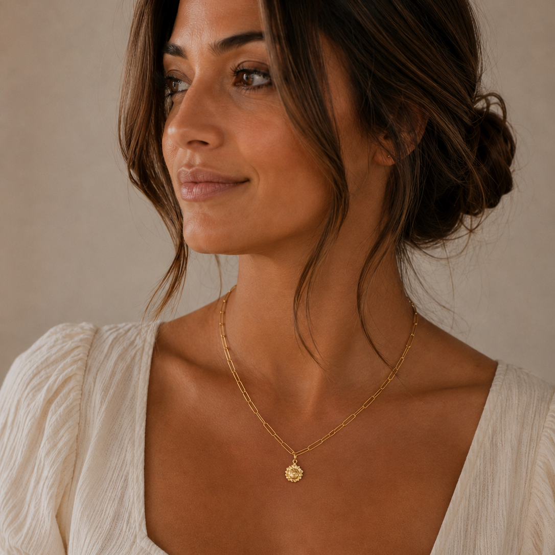 Woman wearing a gold necklace with a beige top against a neutral background