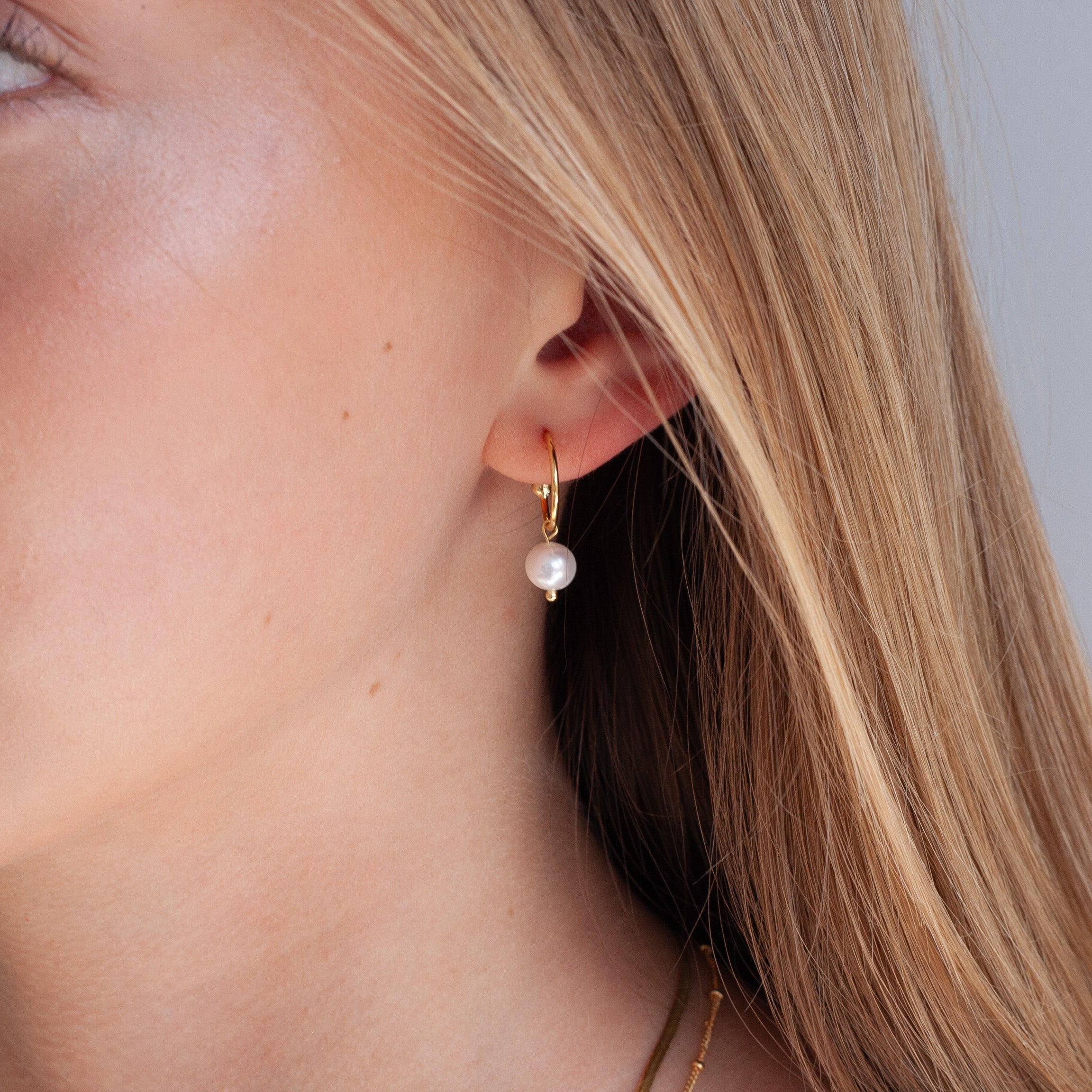Close-up of a woman wearing a pearl earring with a neutral background