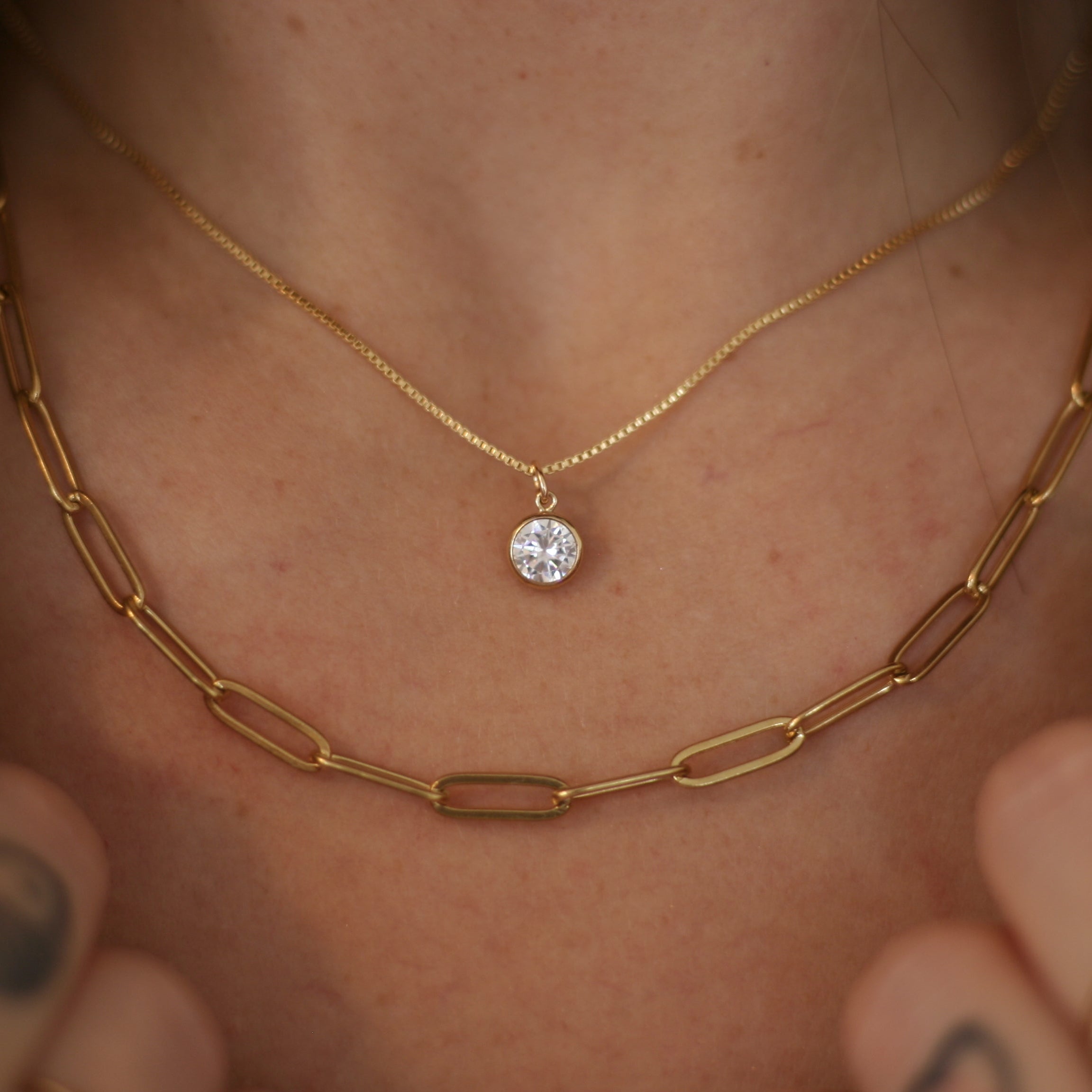 Close-up of a person wearing a gold necklace with a small round pendant.