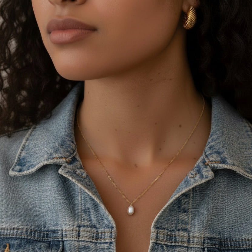 Woman wearing a denim jacket with a pearl pendant
necklace and earrings.