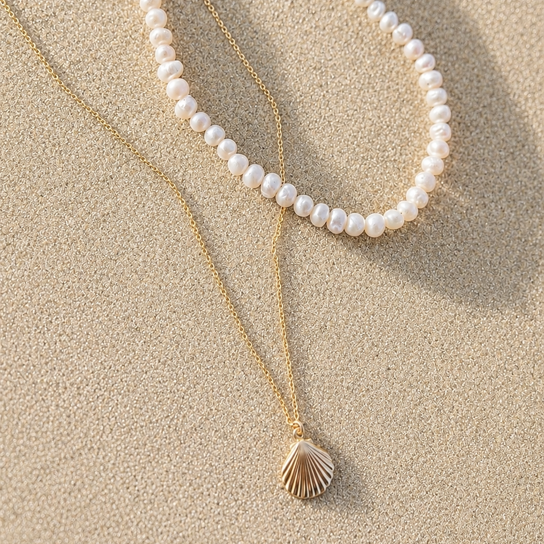 Two necklaces on sand, one pearl and one with a shell pendant