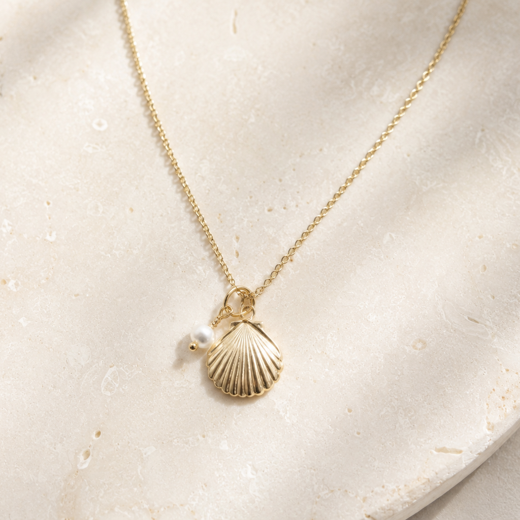 Gold necklace with a shell and pearl pendant on a beige stone surface