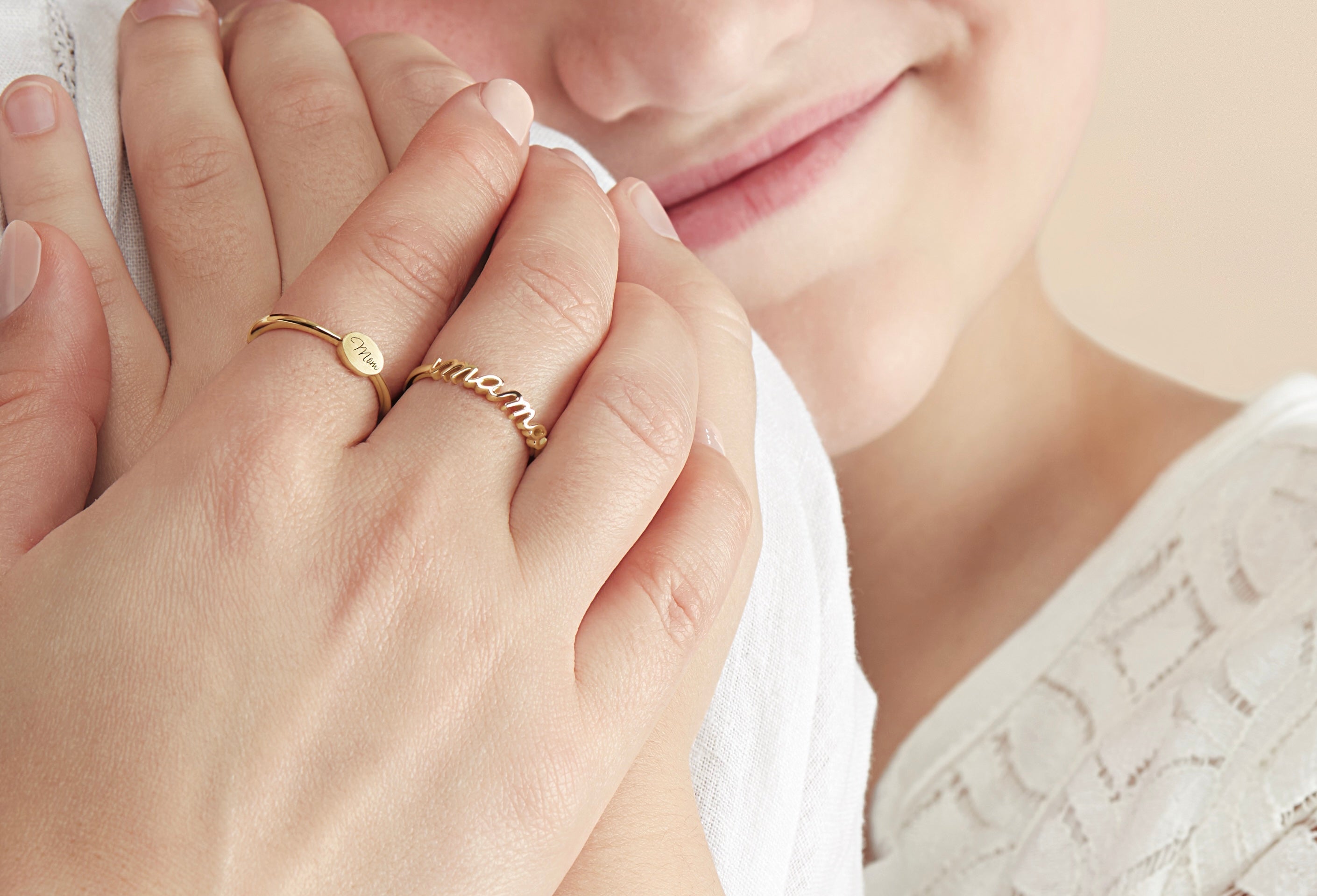 Close-up of hands with gold rings, one with 'mommy' engraved, against a blurred background.