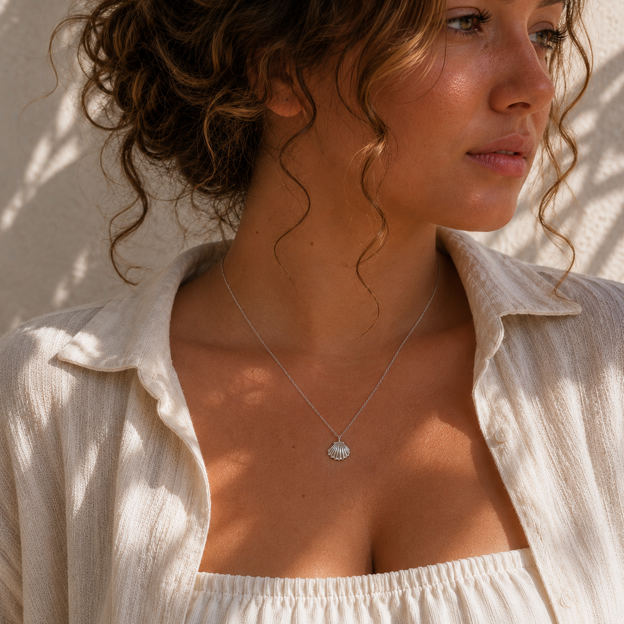 Woman wearing a silver shell pendant necklace with a neutral background