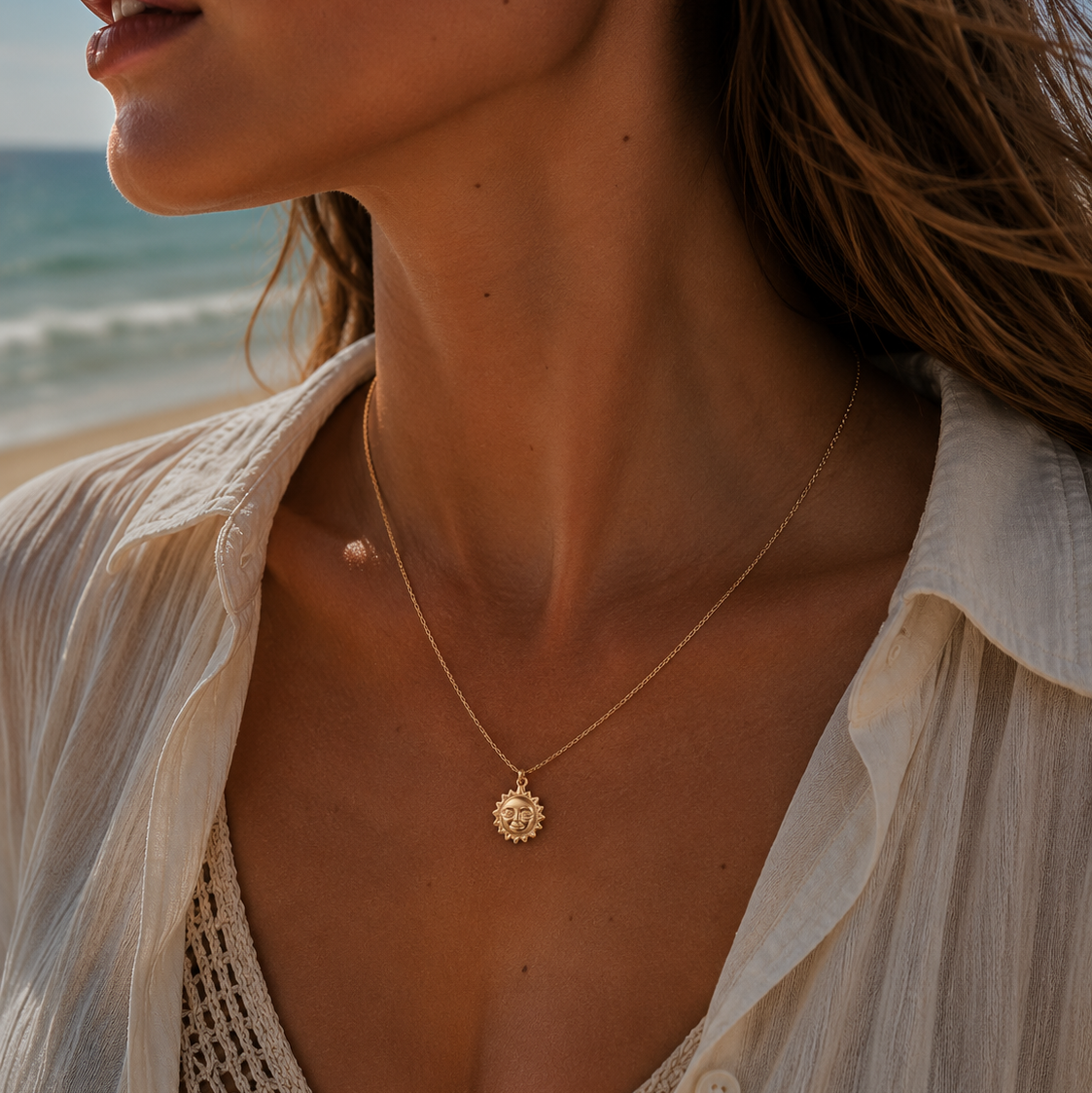 Woman wearing a gold necklace with a sun pendant on a beach.