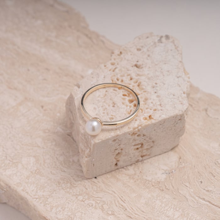 Gold ring with a pearl on a textured stone surface