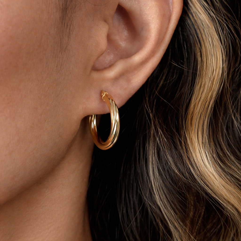 Close-up of a person wearing gold hoop earrings with wavy hair.
