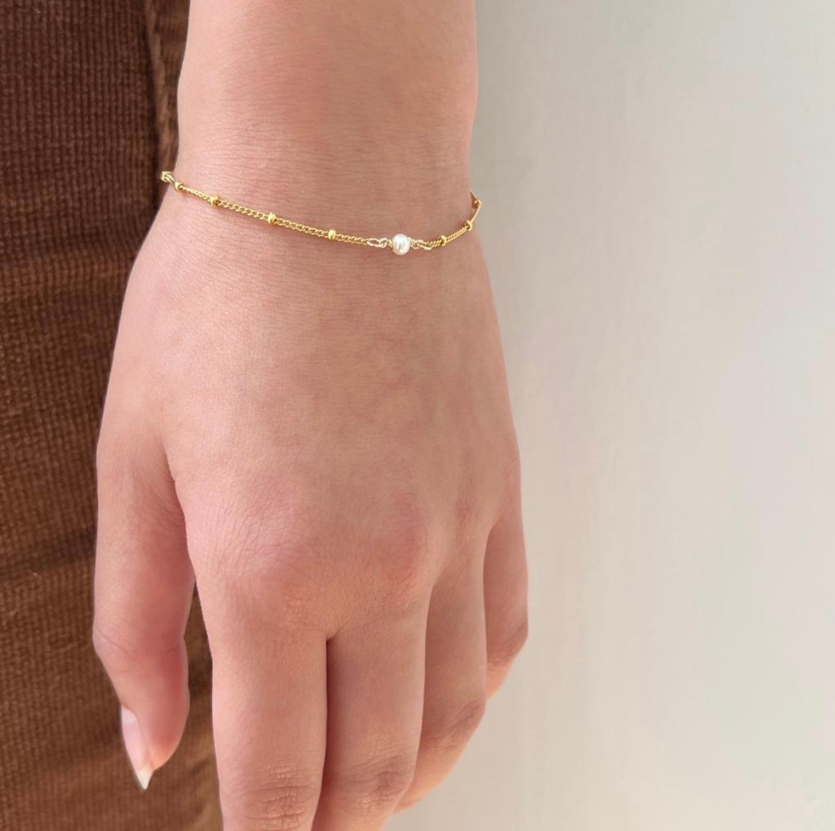 Gold bracelet with a pearl on a hand against a neutral background