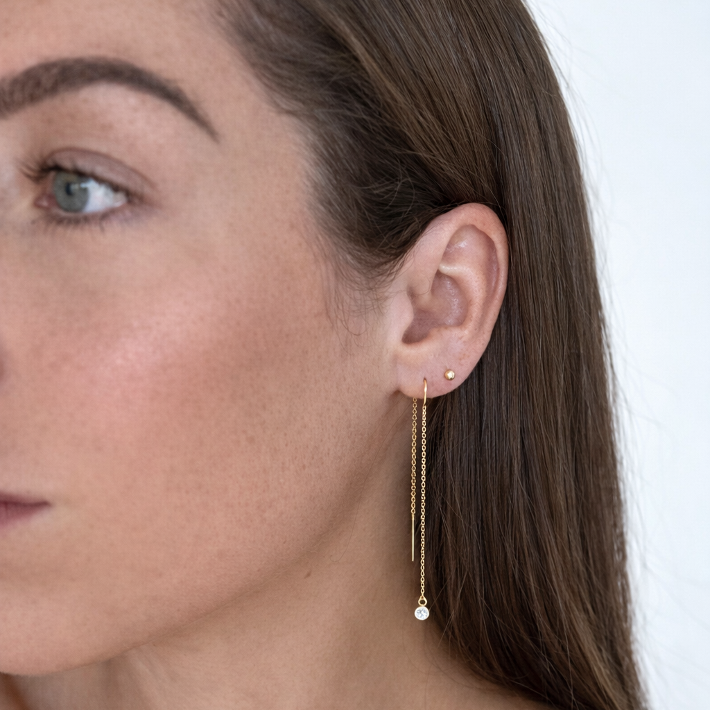 Close-up of a woman wearing a gold earring with a pearl drop against a white background
