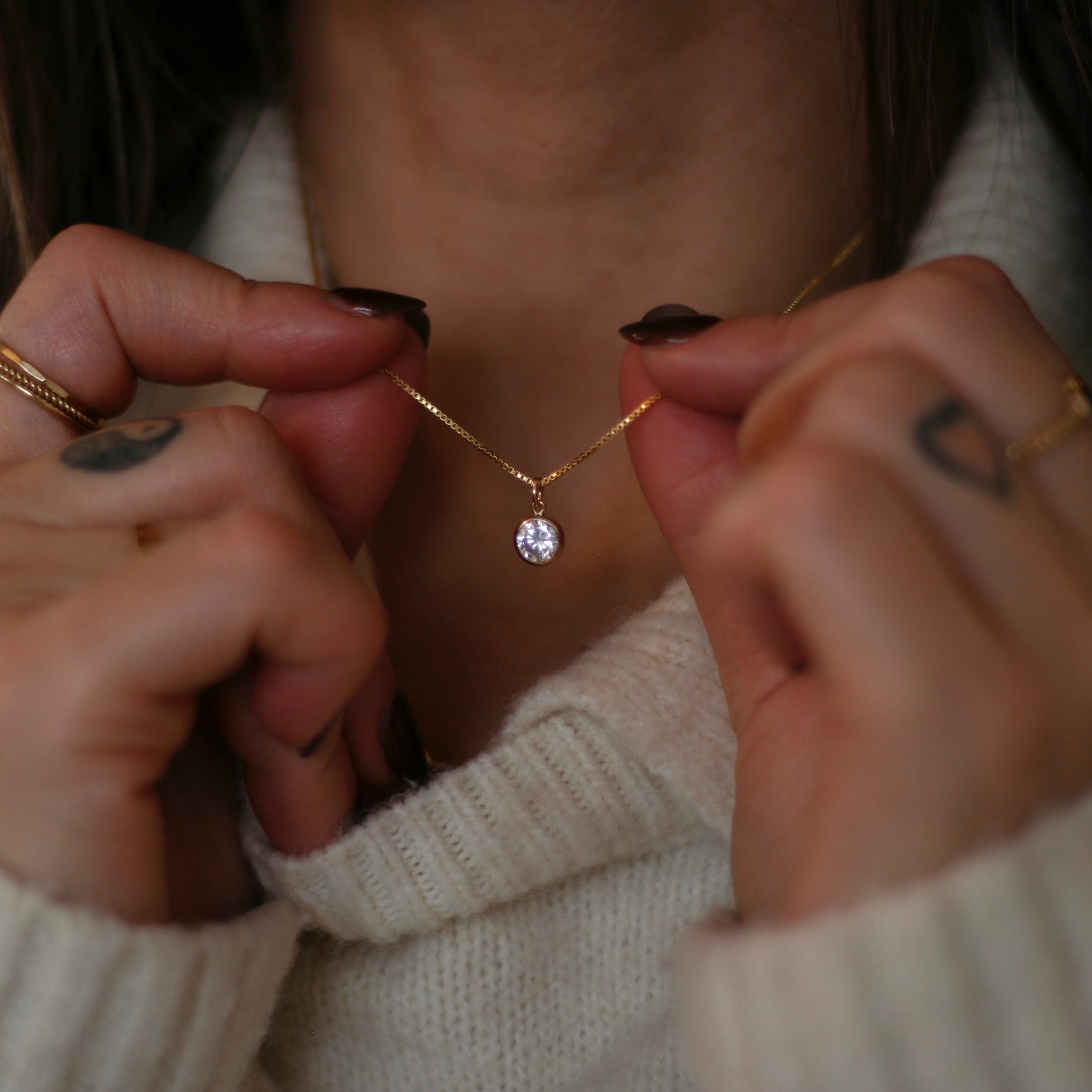 Person adjusting a delicate gold necklace with a clear pendant.