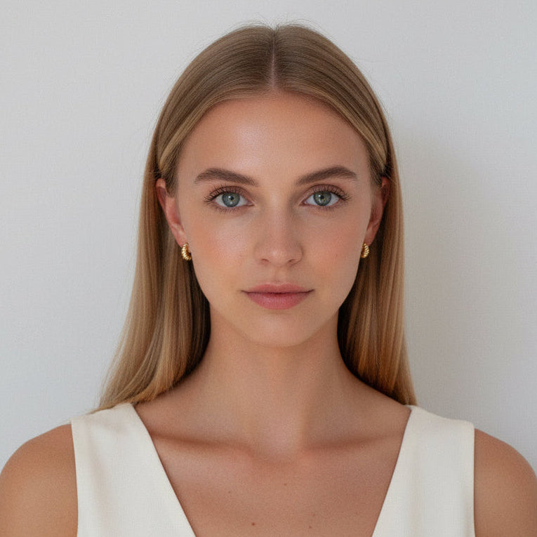 Close-up of a person wearing gold croissant earrings with a neutral background