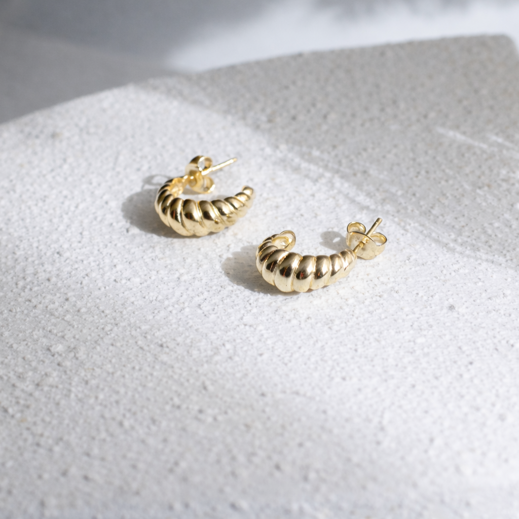 close up of gold vermeil croissant studs on white background
