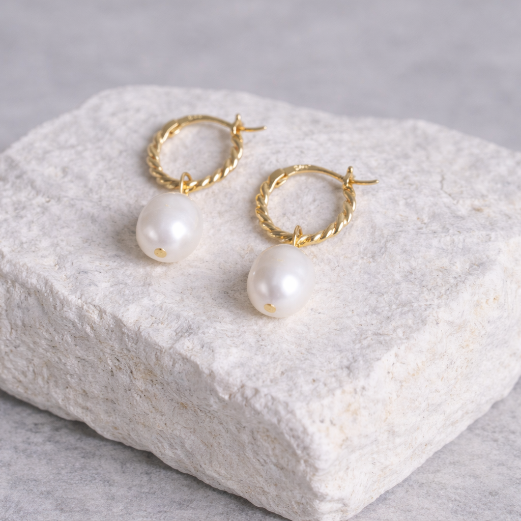 Gold hoop earrings with pearls on a textured white stone