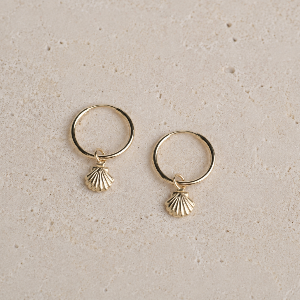 Gold hoop earrings with shell charms on a beige background