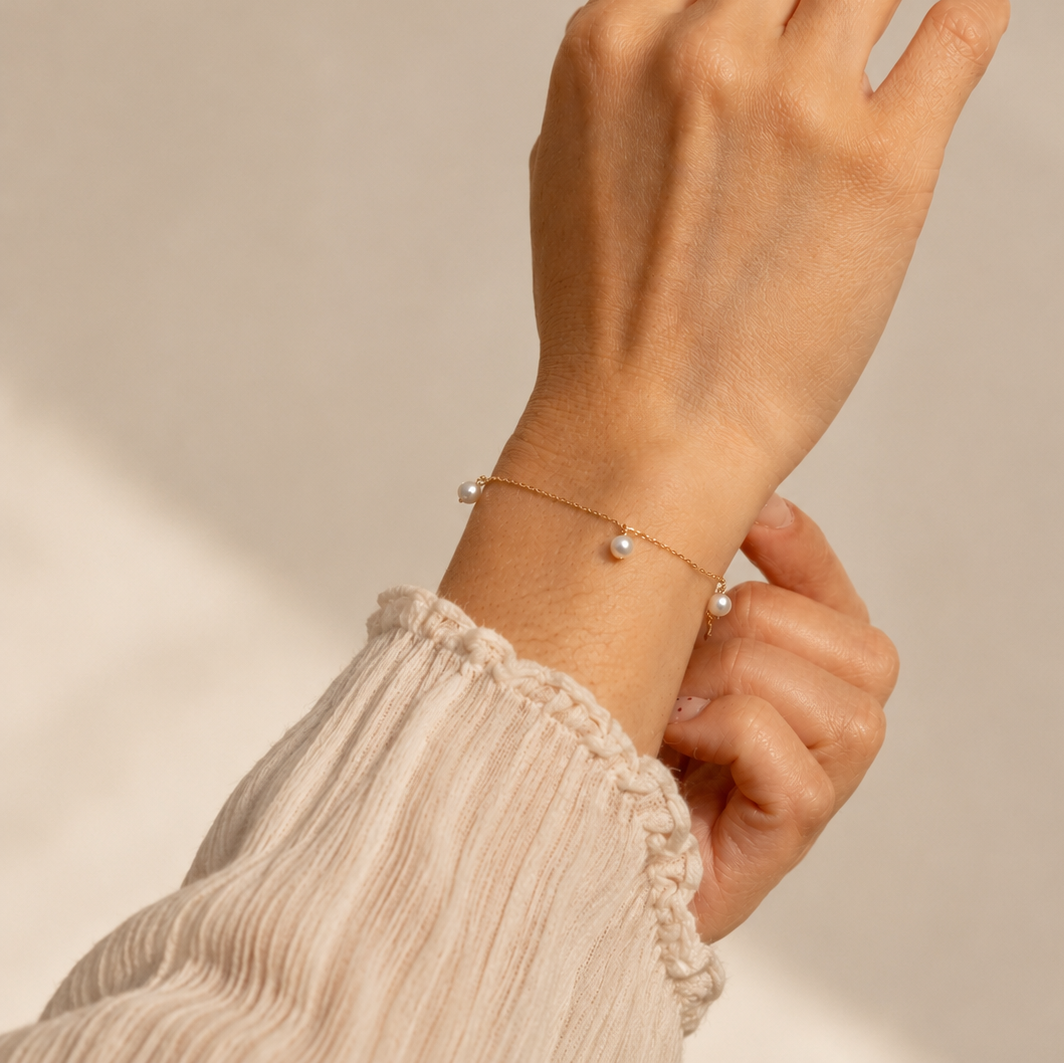 Hand wearing a delicate bracelet with small pearls against a neutral background